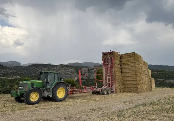 Tractor y pacas apiladas bajo un cielo de tormenta