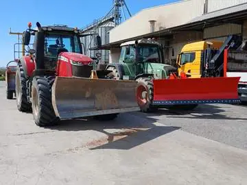 Dos tractores con pala frontal y un camión junto a unos silos