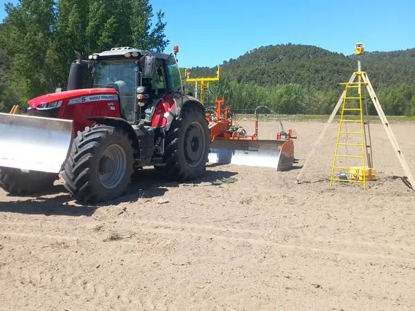 Tractor con niveladora láser y emisor láser sobre trípode